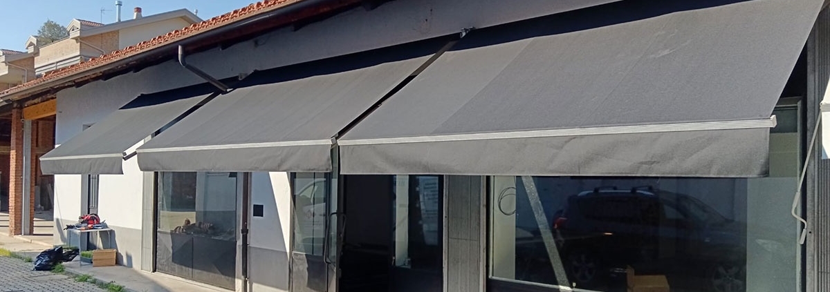 Tenda da sole grigia motorizzata installata sulla facciata di un negozio a Torino con struttura in alluminio e tessuto resistente, protezione solare per l'ingresso